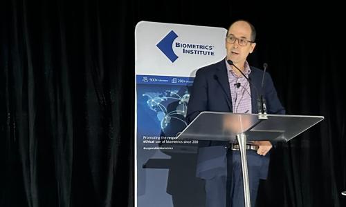 John Shepherd standing at a lectern in front of a vertical banner at the 2024 Biometrics Institute Conference